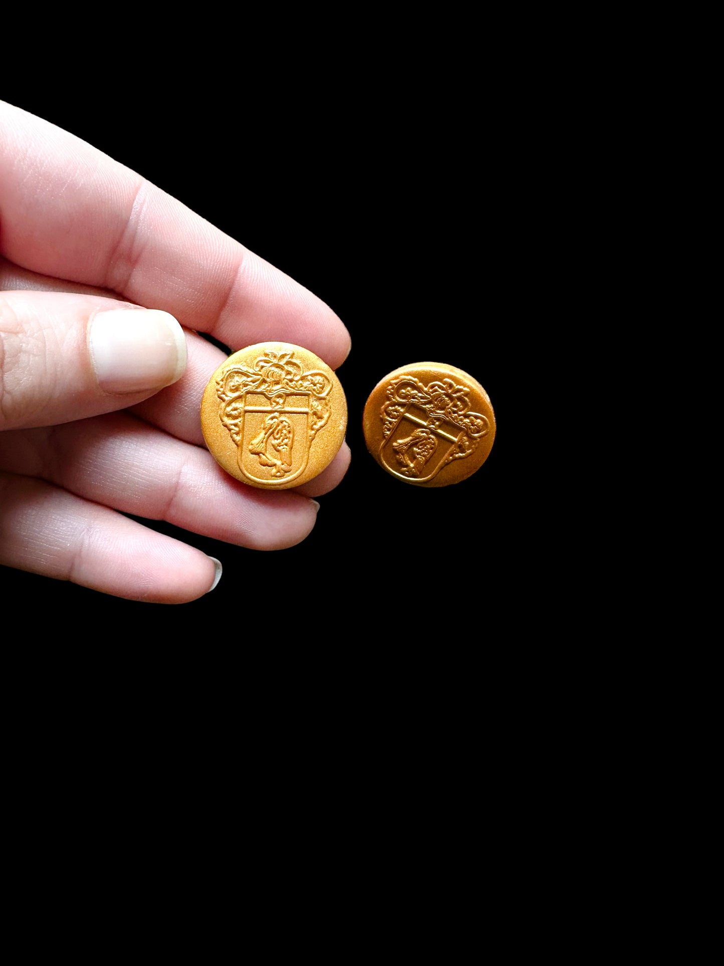 A hand holding gold handmade earrings. These hypoallergenic earrings are embossed with the FLORIT family crest, offering a touch of heritage and elegance to your outfit.