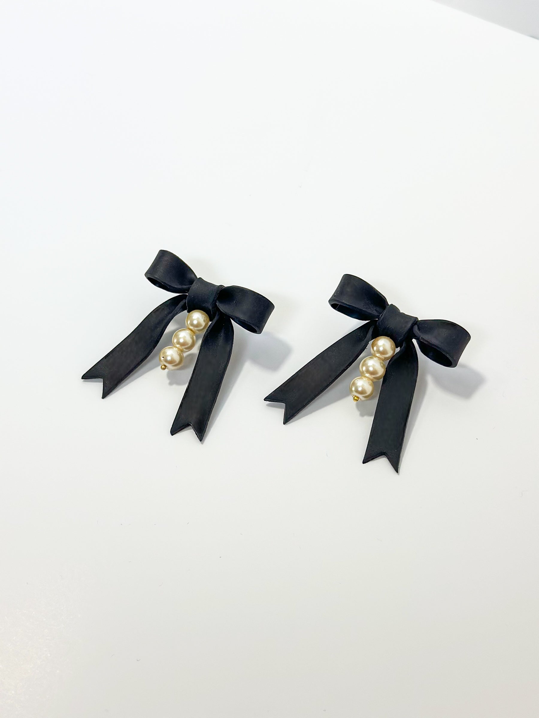 Handmade earrings feature striking black bows that are hand-sculpted and accented with three delicate glass pearls in the center. Hypoallergenic earrings.